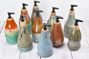 A group of handmade ceramic stoneware soap / lotion bottles with black pumps. Oranges, blues, greens, copper glazes